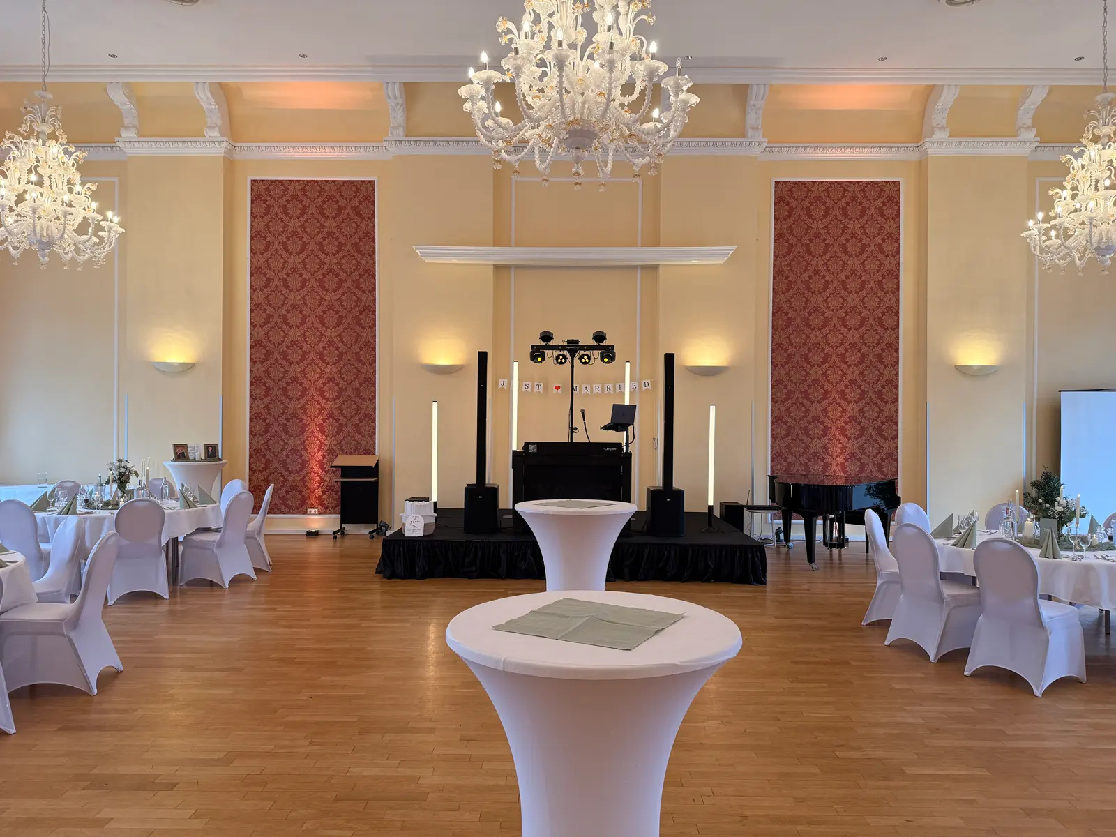 Festsaal im Hotel am Schloss in Aurich mit Kronleuchtern, hohen Wänden und DJ-Bühne bei warmem Ambientelicht