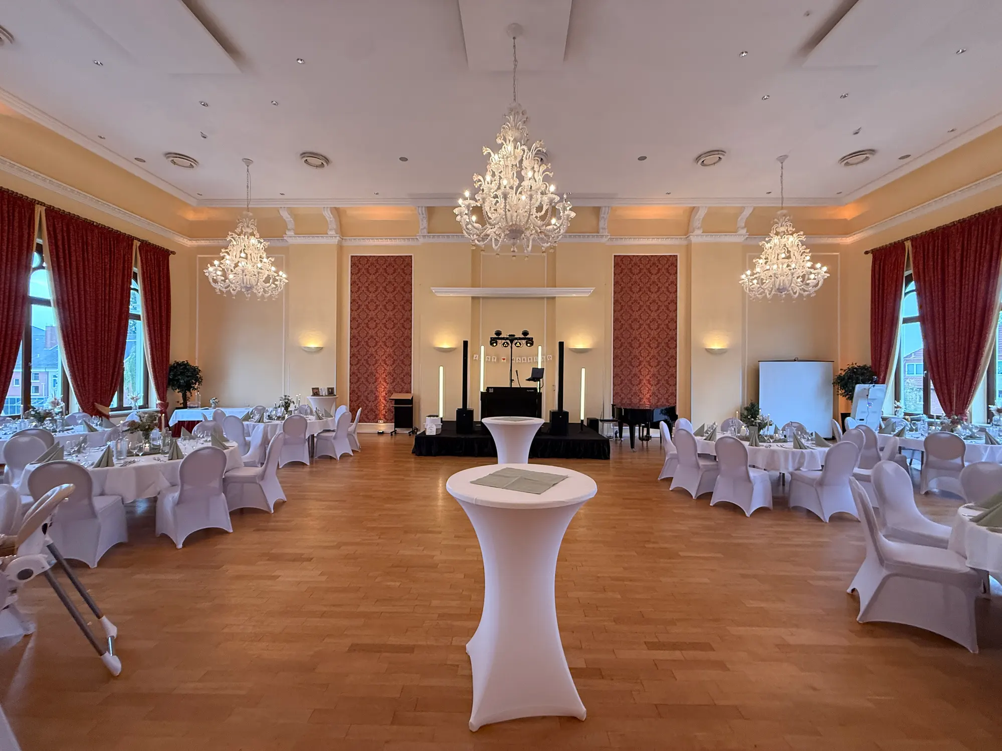 Festlich eingedeckter Saal im Hotel am Schloss in Aurich mit Kronleuchtern, Stuckdecke und DJ-Bühne bei warmem Ambientelicht