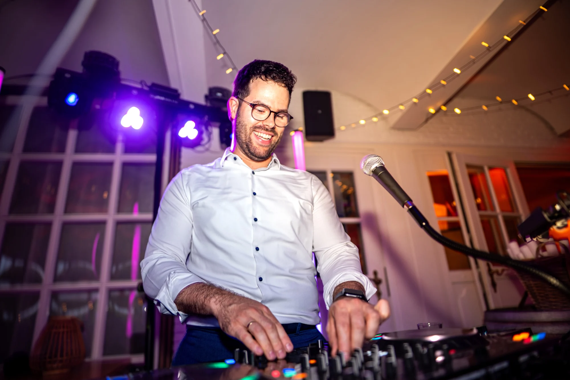 DJ Kai Schmidt lachend am Mischpult vor einer Lichterkette