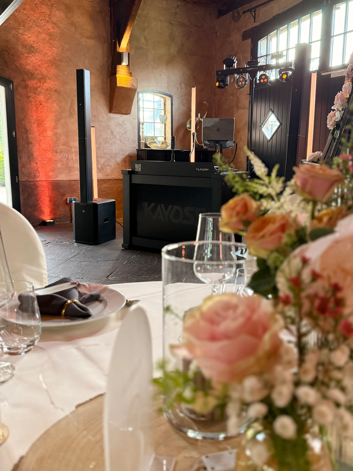 Gedeckte Hochzeitstafel mit Rosen, dahinter das aufgebaute DJ-Pult